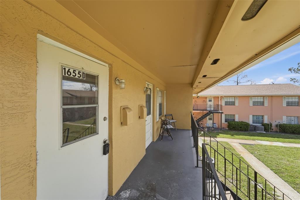 An exterior view of an apartment building walkway with a white door and metal railing — 1655 W OAK RIDGE ROAD UNIT D, ORLANDO, FL