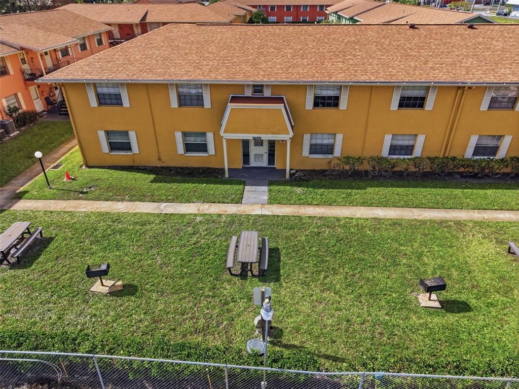 An aerial view shows a yellow two-story apartment building with a grassy courtyard and benches — 1655 W OAK RIDGE ROAD UNIT D, ORLANDO, FL