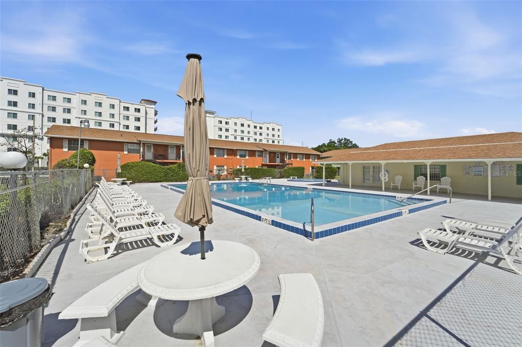 An outdoor swimming pool area with lounge chairs, a table, and surrounding apartment buildings — 1655 W OAK RIDGE ROAD UNIT D, ORLANDO, FL