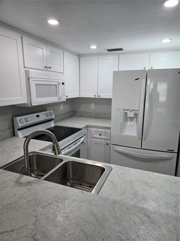 A kitchen features white cabinets, stainless steel appliances, and gray marble-patterned countertops — 4600 MARINE PARKWAY UNIT 107, NEW PORT RICHEY, FL