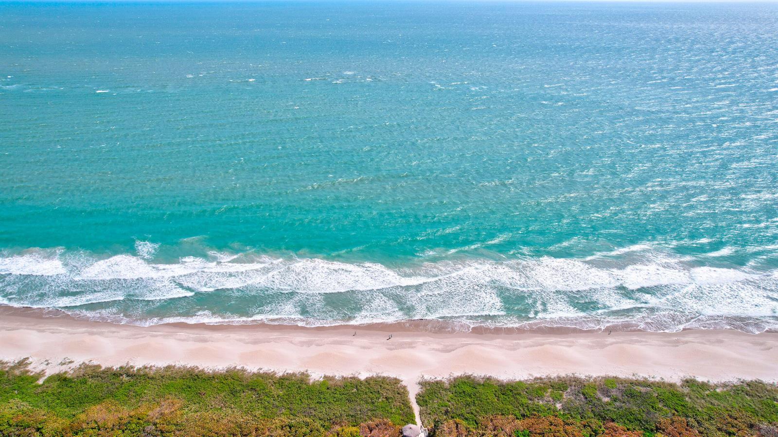 An aerial view of a sandy beach with turquoise ocean waves and coastal vegetation — FORT PIERCE, FL