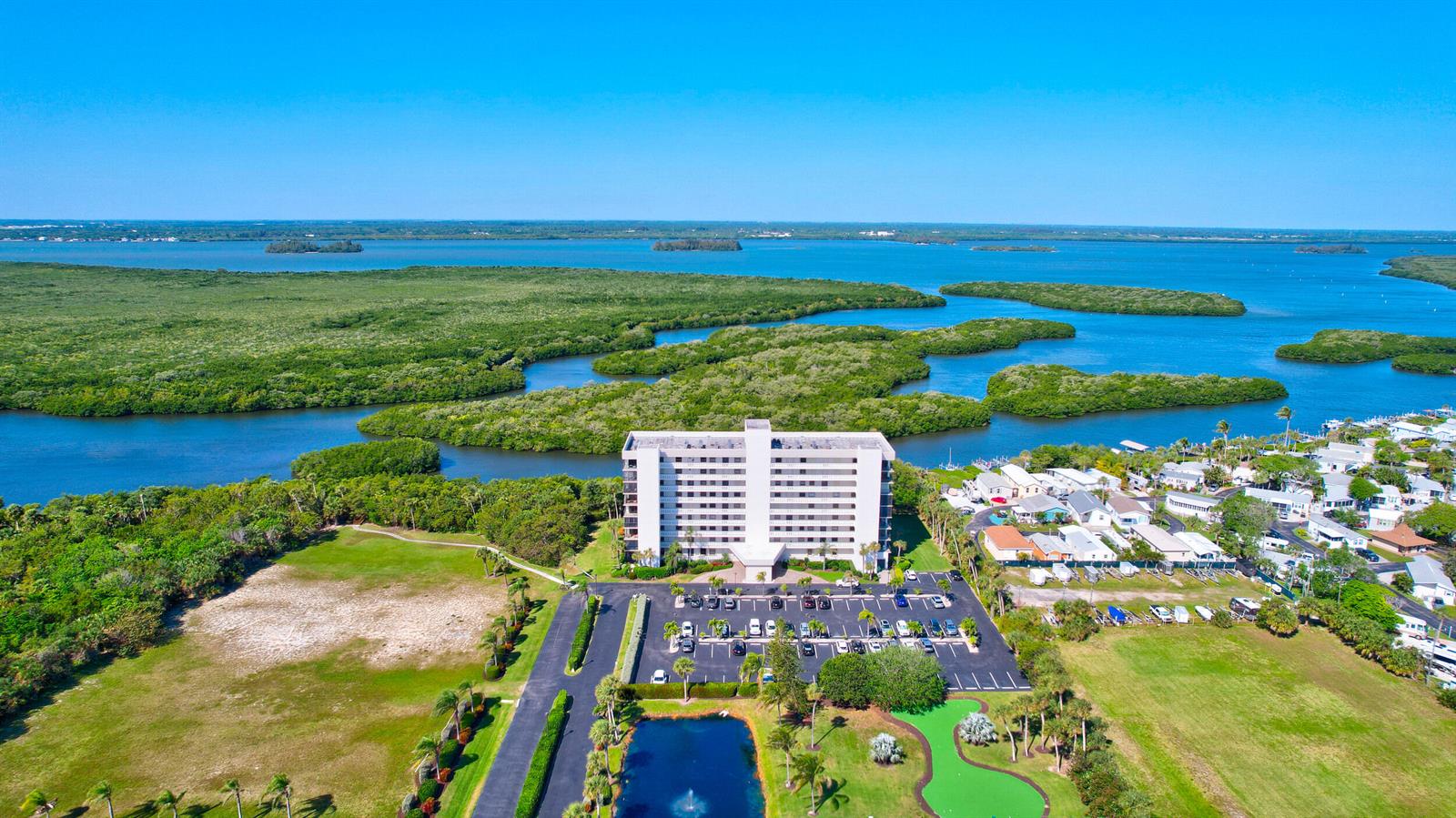 An aerial view shows a tall apartment building surrounded by a parking lot and mangroves — FORT PIERCE, FL