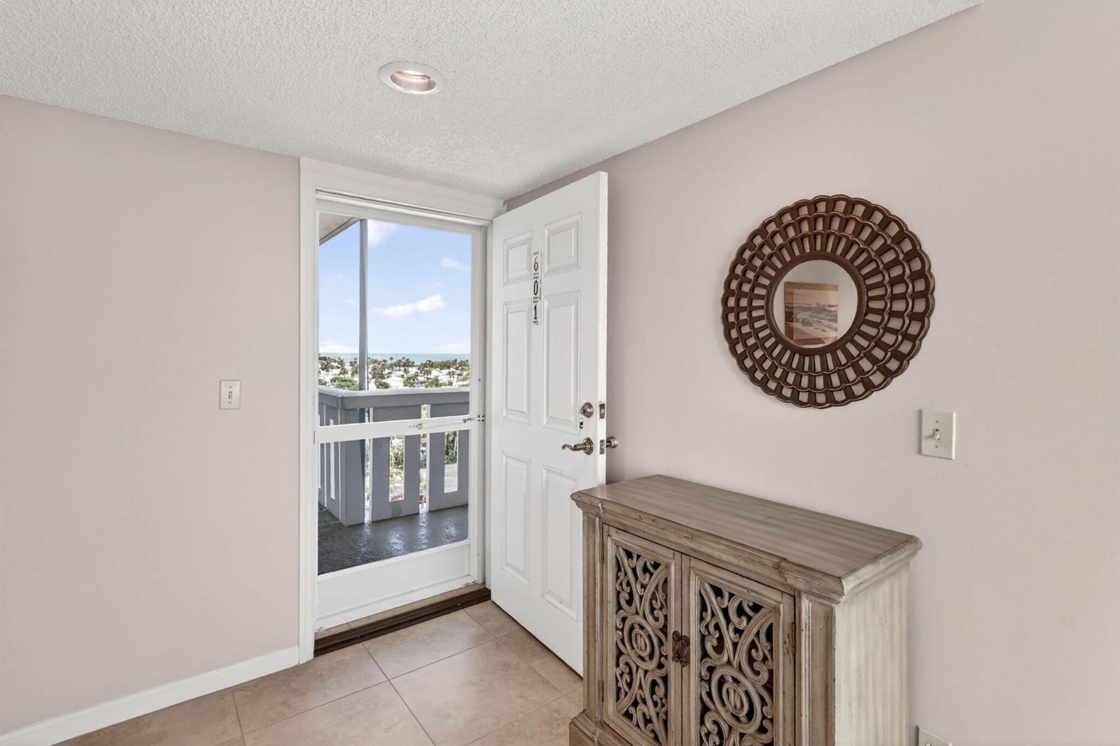 An entryway features a tile floor, a decorative cabinet, a round mirror, and an open door — FORT PIERCE, FL