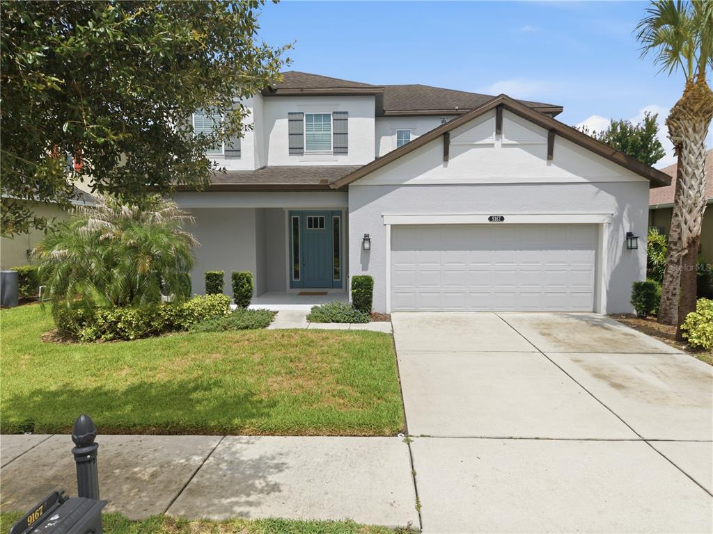 A two-story suburban house features a light gray exterior, a two-car garage, and a blue door — 9167 BELLA VITA CIRCLE, LAND O LAKES, FL