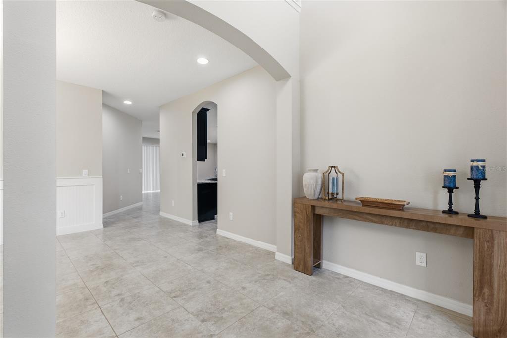 A hallway with light tile flooring leads toward a kitchen with dark cabinets — 9167 BELLA VITA CIRCLE, LAND O LAKES, FL