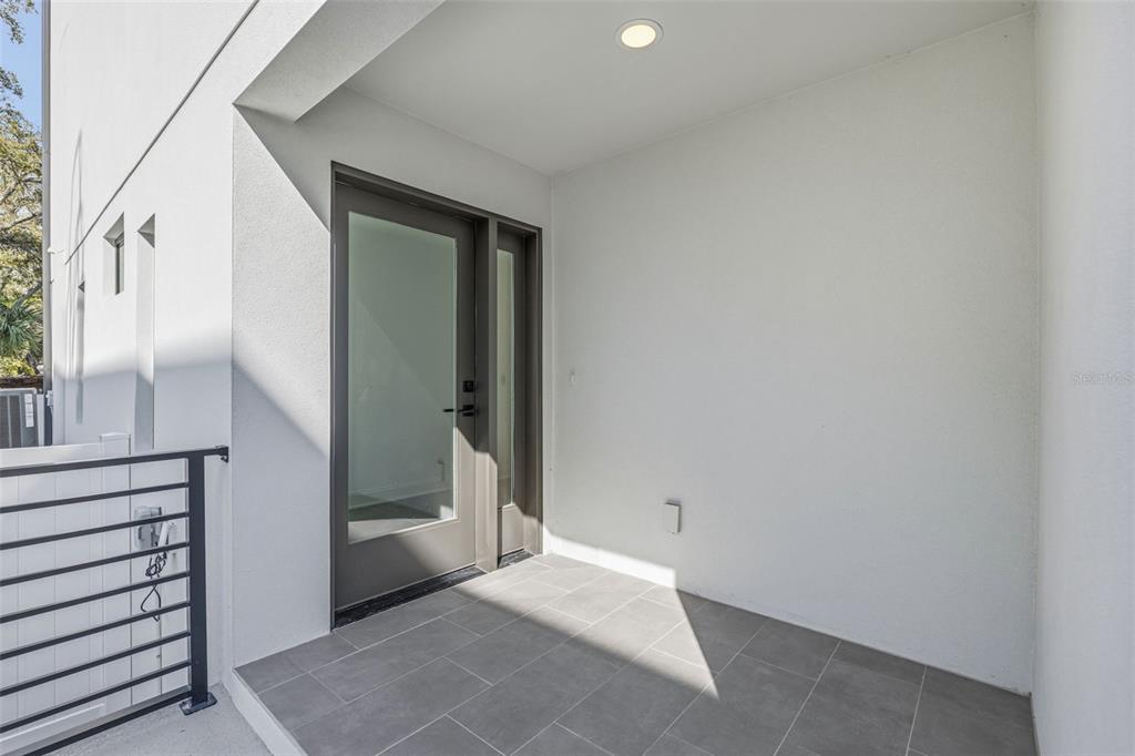 A covered patio features gray tile flooring, white walls, and a glass-paneled entry door — 4509 W NORTH A STREET UNIT 2, TAMPA, FL