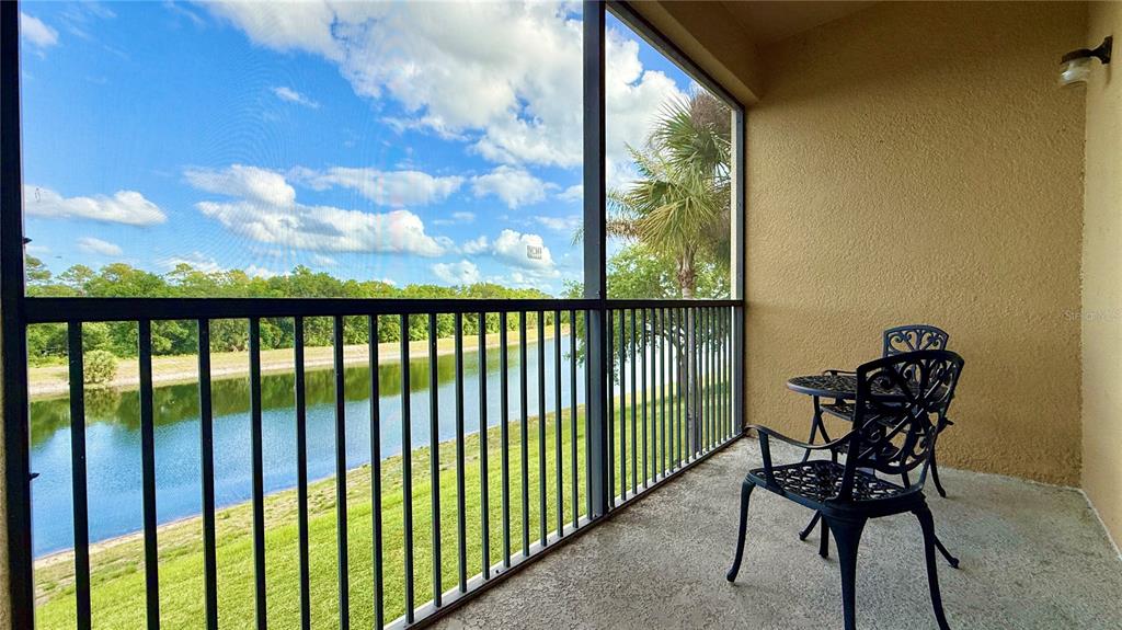 A screened-in balcony features a small table and two chairs overlooking a pond — 2831 OAKWATER DRIVE UNIT 2831, KISSIMMEE, FL