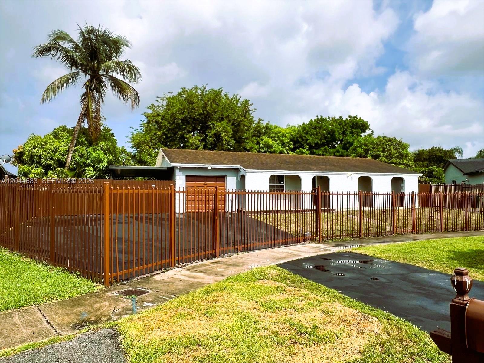 A single-story house with a brown roof and a metal fence in the front yard — 26080 SW 132nd Pl, Homestead FL 33032, HOMESTEAD, FL