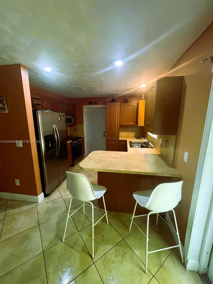 A kitchen features wood cabinets, a breakfast bar with two chairs, and tile flooring — 26080 SW 132nd Pl, Homestead FL 33032, HOMESTEAD, FL
