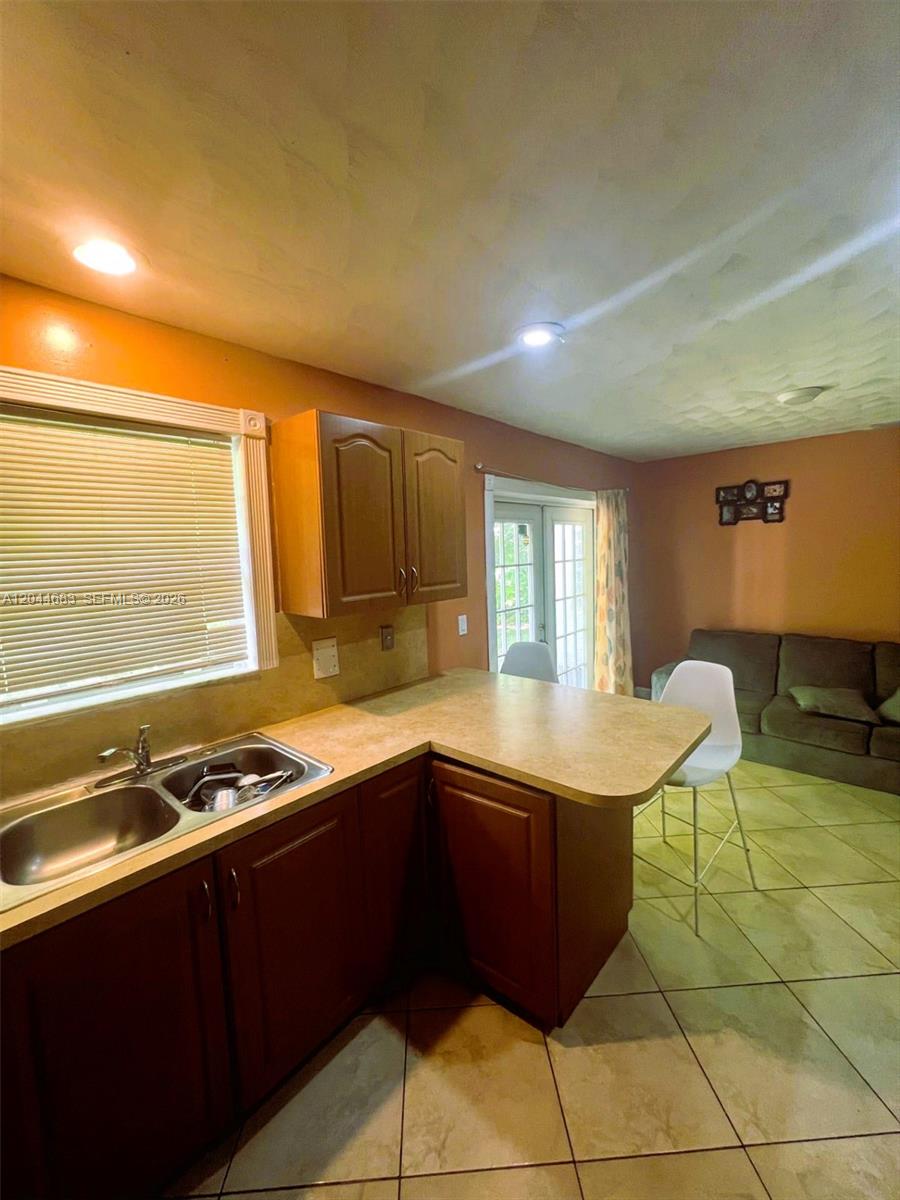 A kitchen with wood cabinets, a double sink, and a breakfast bar overlooks a living area — 26080 SW 132nd Pl, Homestead FL 33032, HOMESTEAD, FL