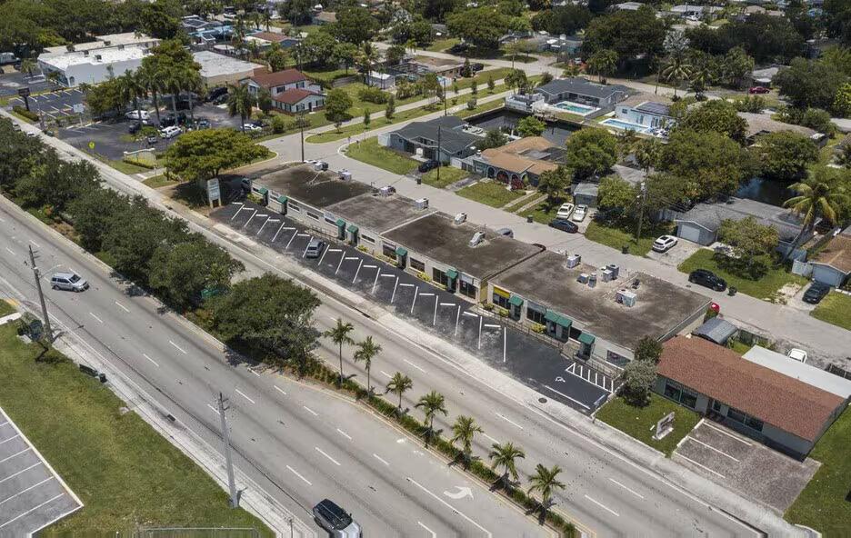 An aerial view of a single-story commercial strip mall with a parking lot and road — OAKLAND PARK, FL