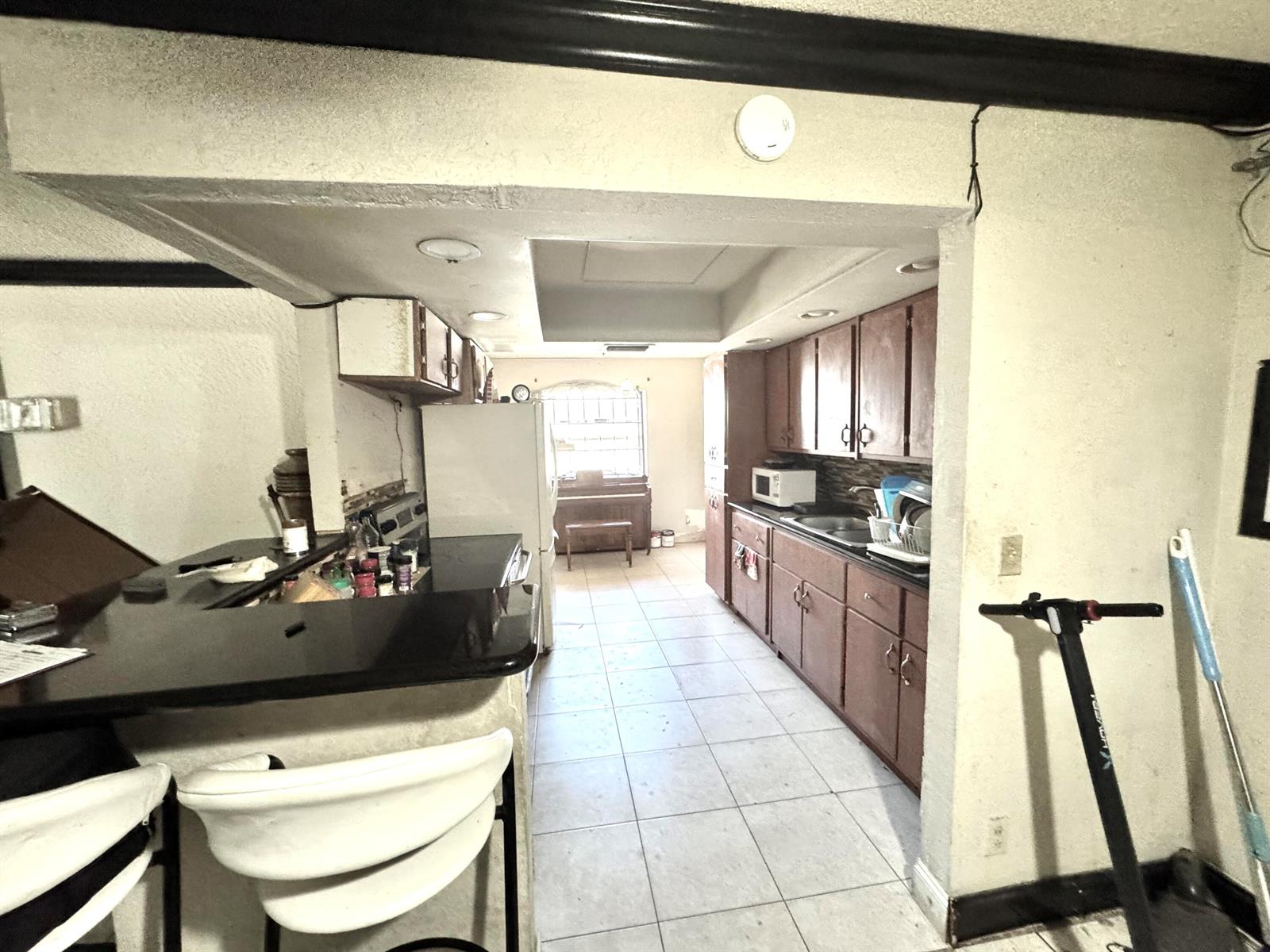 A kitchen features dark wood cabinets, black countertops, and a breakfast bar with white stools — 4310 NE 1st Terrace, Pompano Beach FL 33064, POMPANO BEACH, FL
