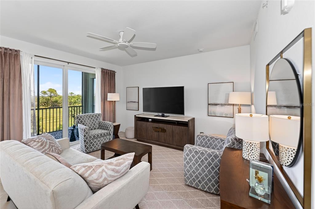 A living room features a sofa, two patterned armchairs, a television console, and a balcony — 12320 WELLEN GOLF STREET UNIT 306, VENICE, FL
