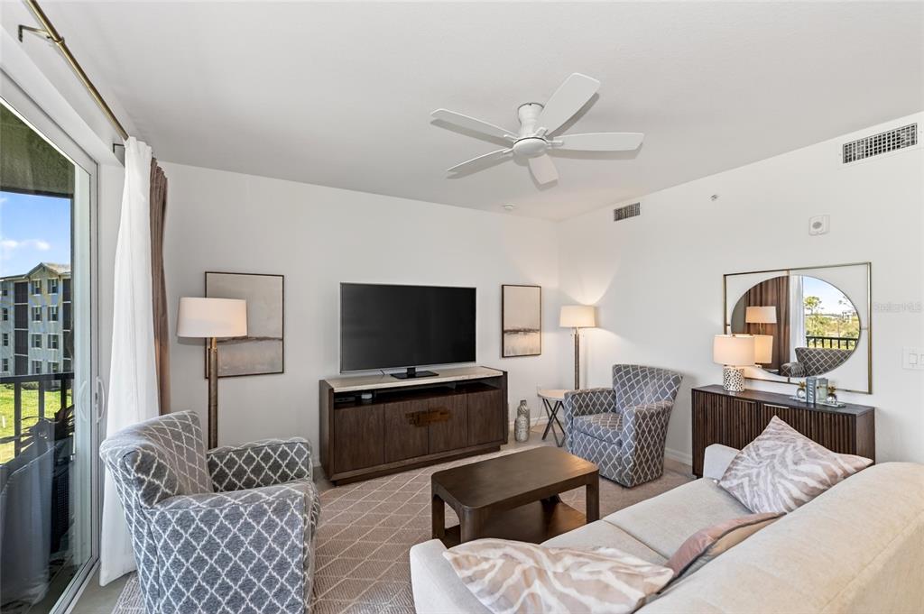 A living room features a television, two patterned armchairs, a sofa, and a sliding door — 12320 WELLEN GOLF STREET UNIT 306, VENICE, FL