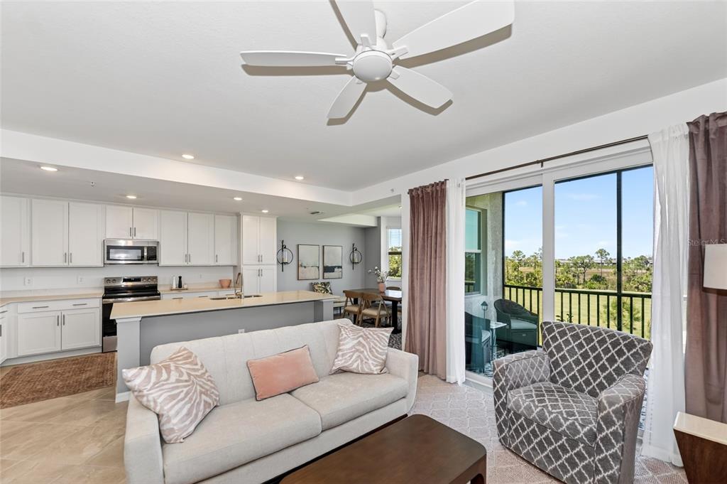 An open-concept living room and kitchen featuring white cabinetry, a ceiling fan, and balcony access — 12320 WELLEN GOLF STREET UNIT 306, VENICE, FL