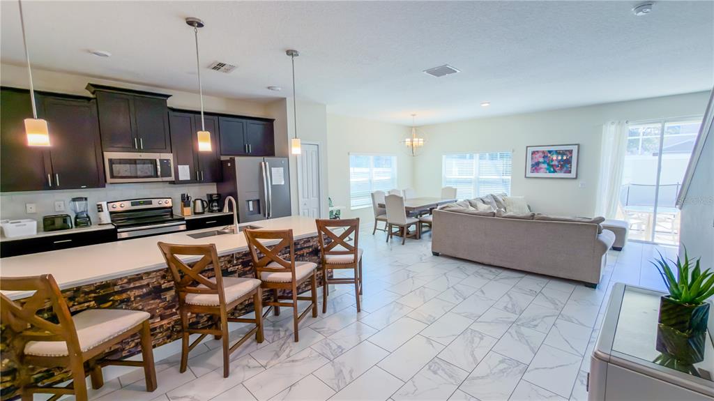 An open-concept kitchen and living area features dark cabinetry, a stone-faced island, and tile flooring — 444 OCEAN COURSE AVENUE, DAVENPORT, FL