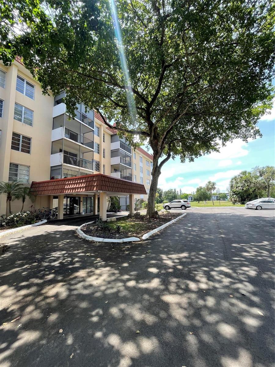 An exterior view of a multi-story apartment building with a covered entrance and large tree — 4158 Inverrary Drive # 111, Lauderhill FL 33319, LAUDERHILL, FL