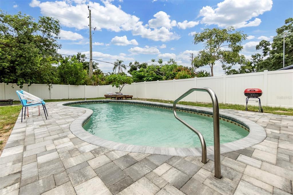 A backyard features a kidney-shaped swimming pool surrounded by a paver patio and white fencing — 2714 42ND STREET W, BRADENTON, FL