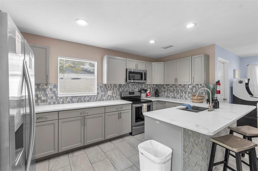 A modern kitchen features gray cabinets, a white island, stainless steel appliances, and tiled backsplash — 2714 42ND STREET W, BRADENTON, FL
