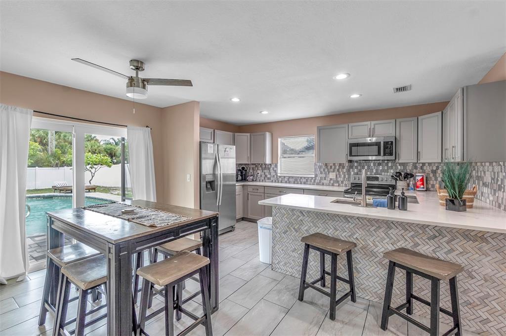 A kitchen with gray cabinets, a tiled island, and a dining area overlooking a pool — 2714 42ND STREET W, BRADENTON, FL