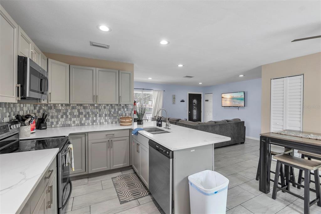 A kitchen with gray cabinets, white countertops, and a tile backsplash opens to a living area — 2714 42ND STREET W, BRADENTON, FL