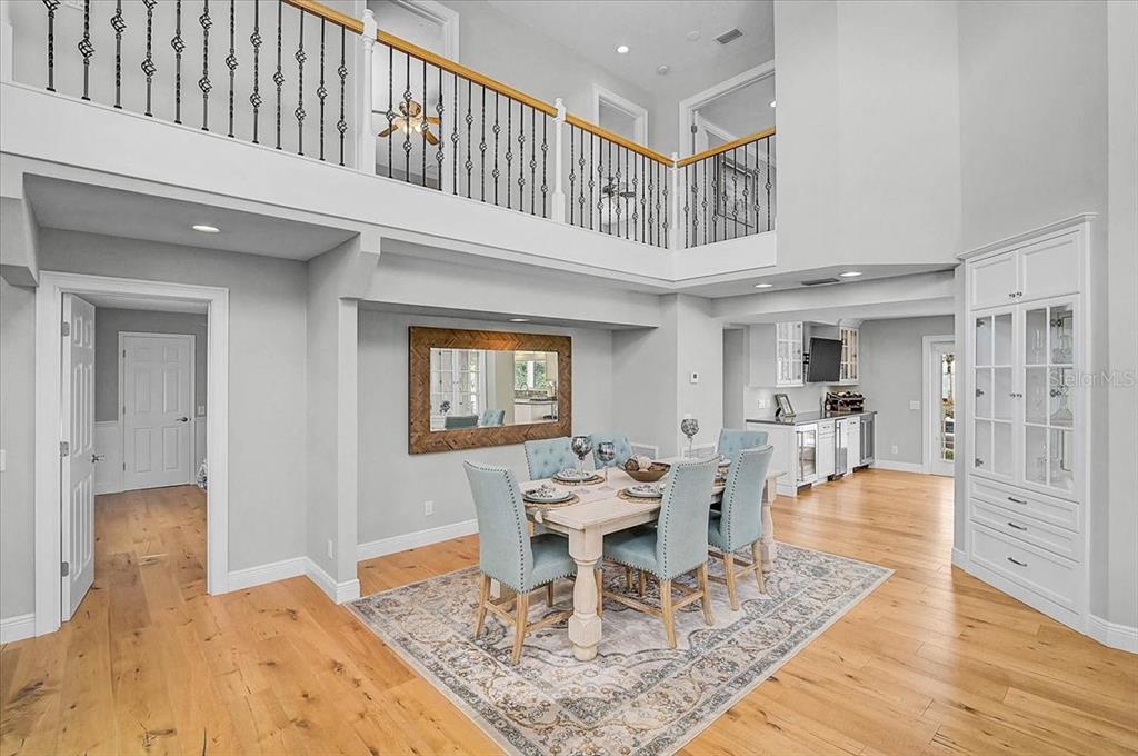 An open-concept living and dining area features vaulted ceilings, hardwood floors, and light-colored furnishings — 320 RINGLING POINT DRIVE, SARASOTA, FL