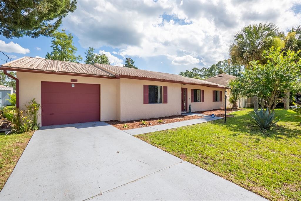 A single-story house with a tan stucco exterior, a red garage door, and a metal roof — 25 ETHAN ALLEN DRIVE, PALM COAST, FL