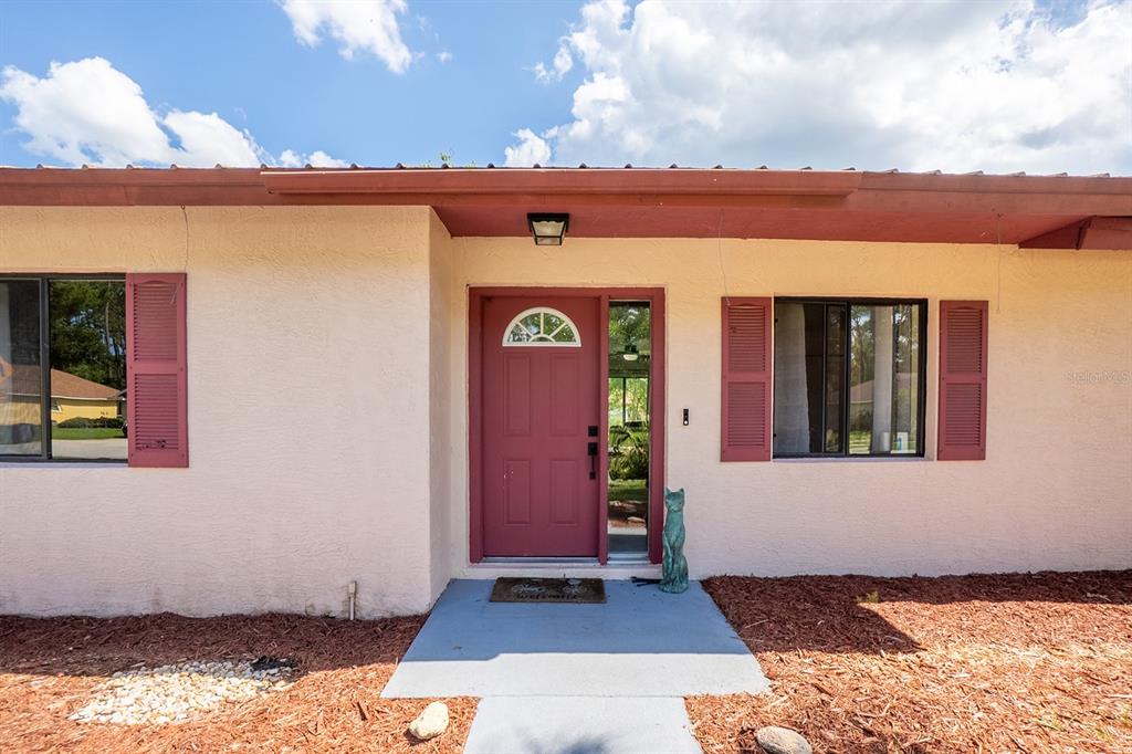 The exterior of a house features a red front door, shutters, and a concrete walkway — 25 ETHAN ALLEN DRIVE, PALM COAST, FL