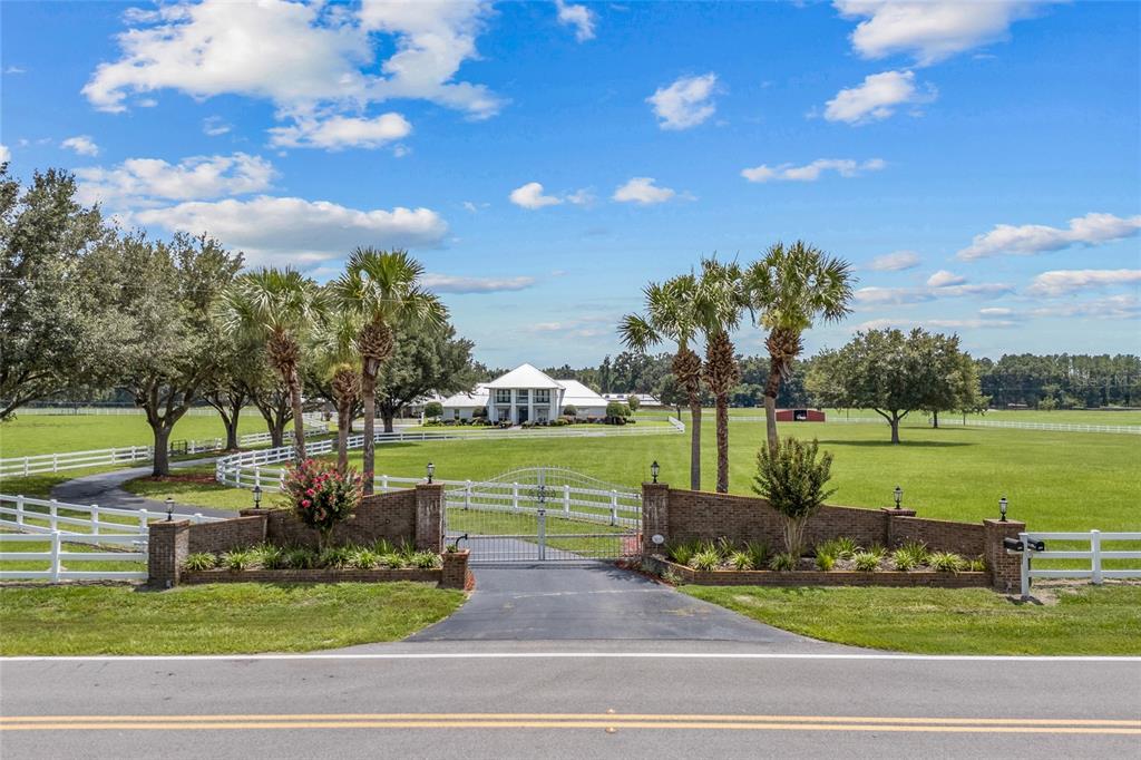 A gated entrance with brick pillars leads to a white house set on a large lawn — 550 SW GABRIEL PLACE, LAKE CITY, FL