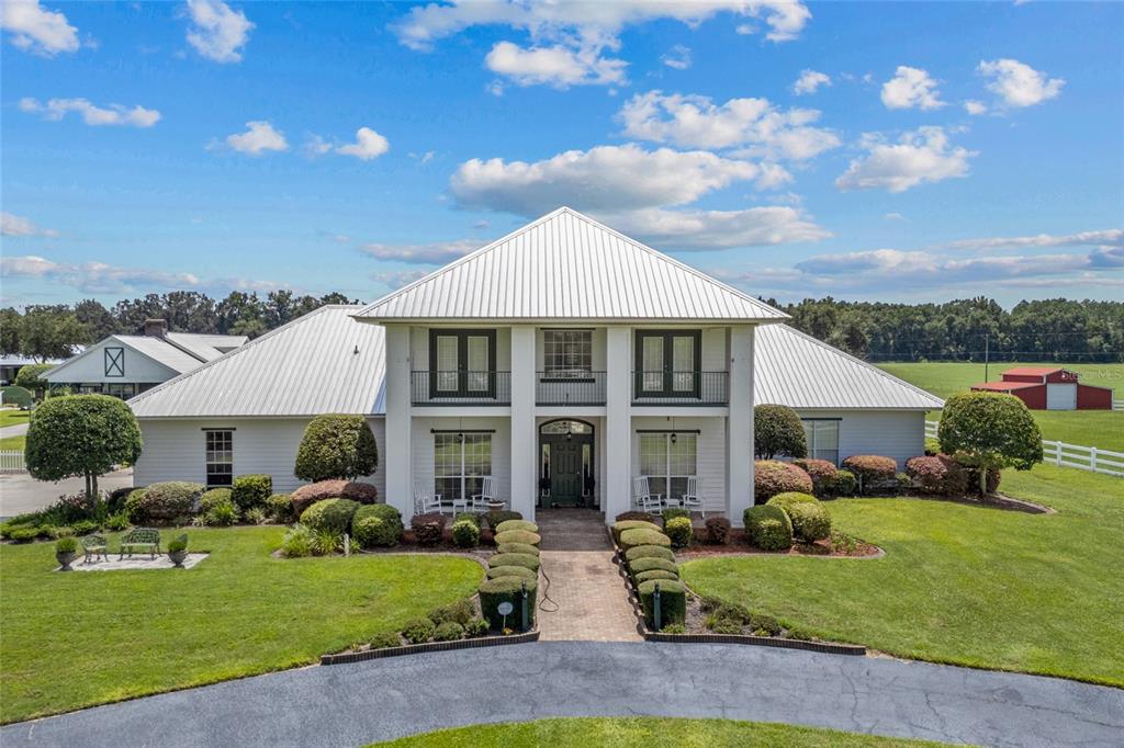 A two-story white house with a metal roof features a paved walkway and landscaped lawn — 550 SW GABRIEL PLACE, LAKE CITY, FL