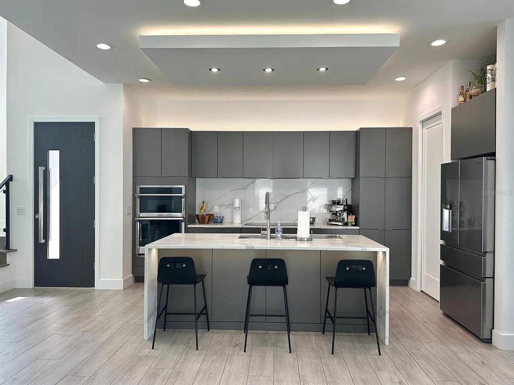 A modern kitchen features dark gray cabinetry, a marble-topped island, and three black bar stools — 4217 W ARCH STREET, TAMPA, FL