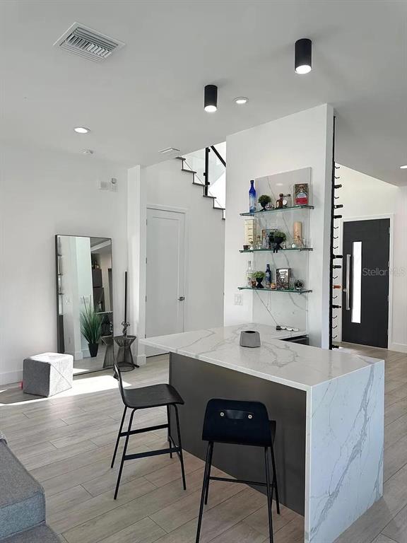 A modern kitchen features a marble-topped island, bar stools, and a glass-shelved wall display — 4217 W ARCH STREET, TAMPA, FL