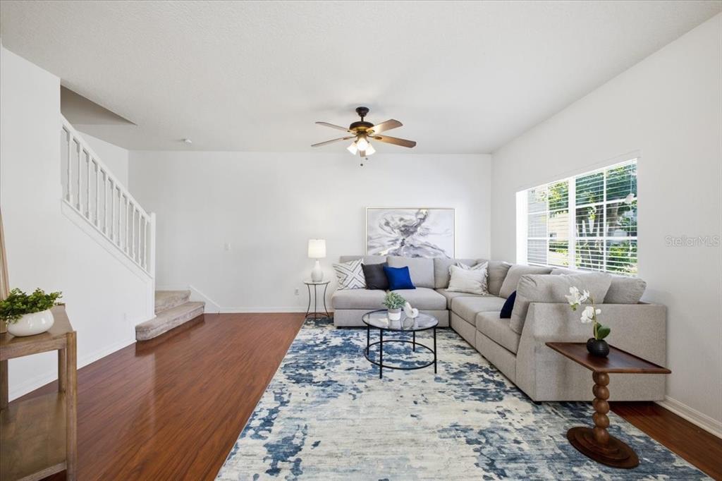 A living room features a grey sectional sofa, a blue patterned rug, and wooden flooring — 233 CAPE HARBOUR LOOP UNIT 107, BRADENTON, FL