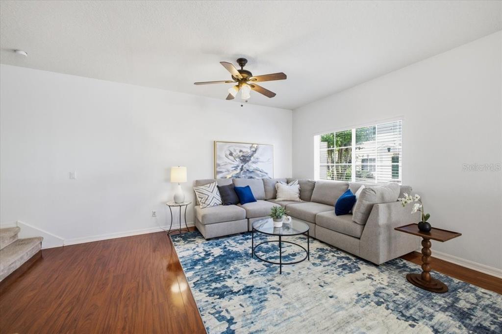 A living room features a gray sectional sofa, a blue patterned rug, and wood flooring — 233 CAPE HARBOUR LOOP UNIT 107, BRADENTON, FL