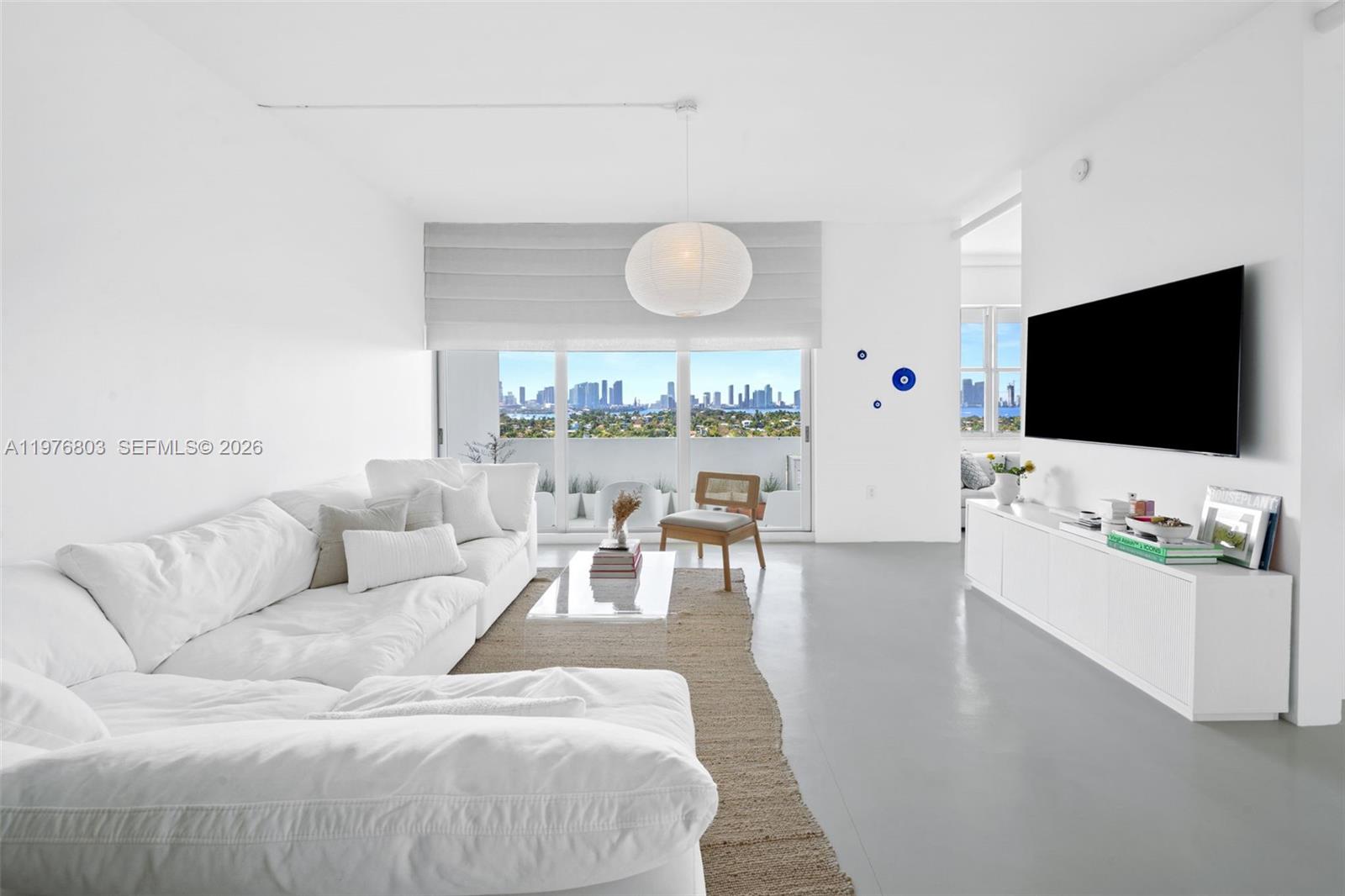 A bright living room features a white sectional sofa, a television, and a city view — 3 Island Ave # G, Miami Beach FL 33139, MIAMI BEACH, FL
