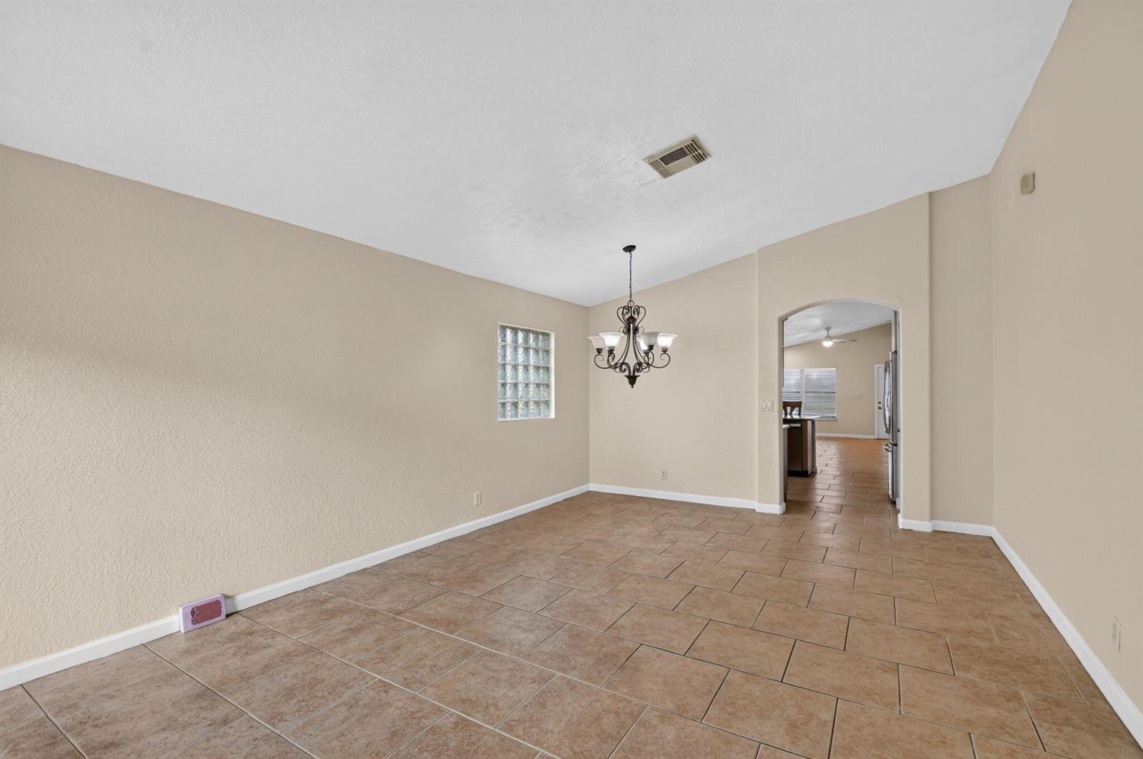 An empty dining room features tan tile flooring, a glass block window, and a chandelier — 1107 Big Torch Street, Riviera Beach FL 33407, RIVIERA BEACH, FL