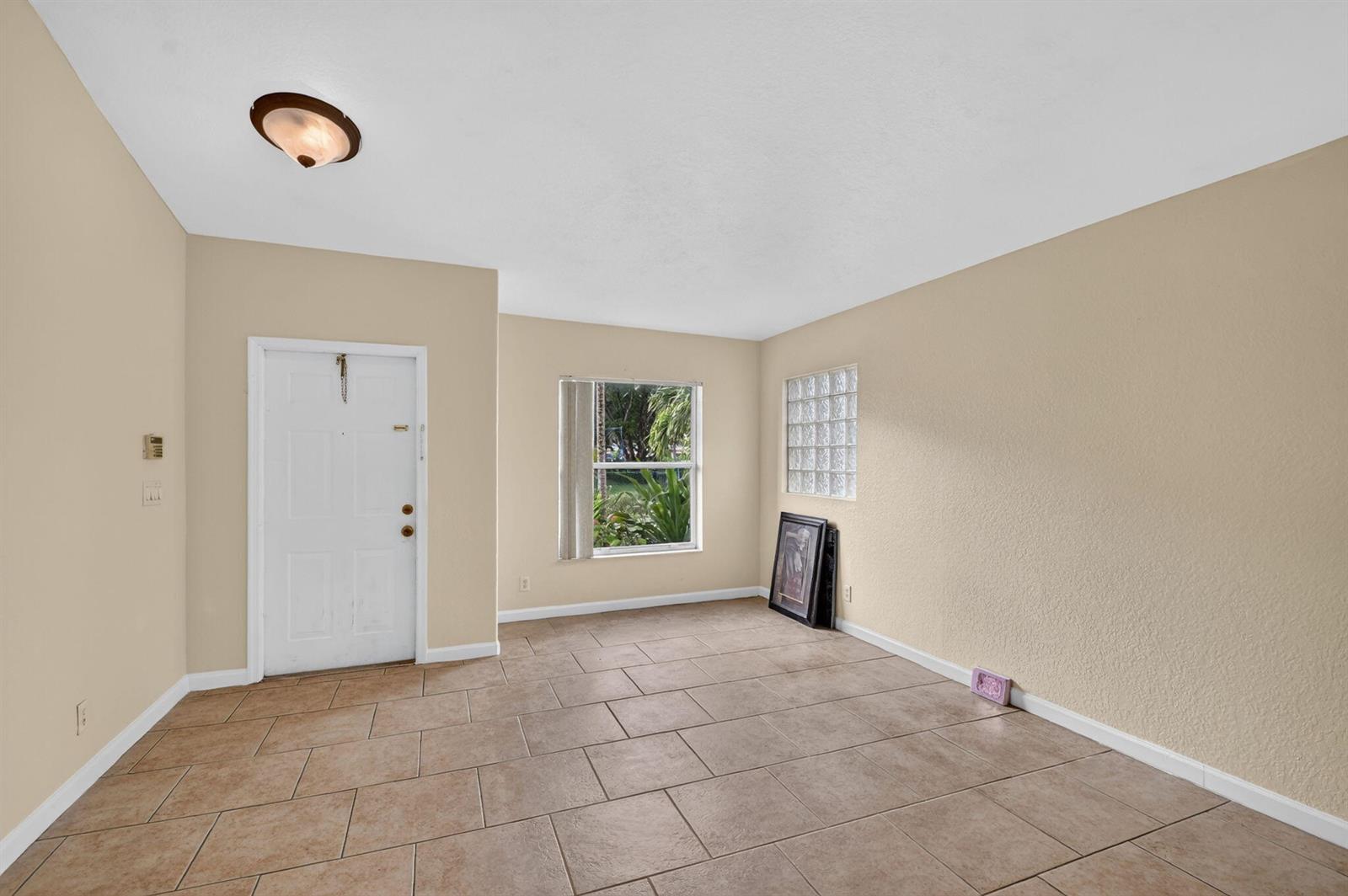 An empty room with beige walls, tile flooring, a white door, and glass block windows — 1107 Big Torch Street, Riviera Beach FL 33407, RIVIERA BEACH, FL
