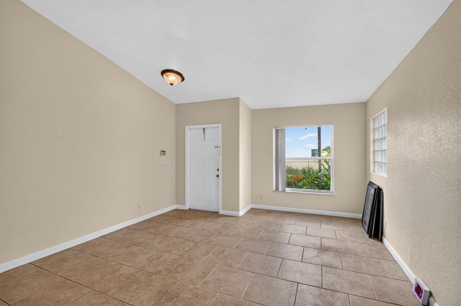 An empty room with beige walls, tile flooring, a white door, and a large window — 1107 Big Torch Street, Riviera Beach FL 33407, RIVIERA BEACH, FL