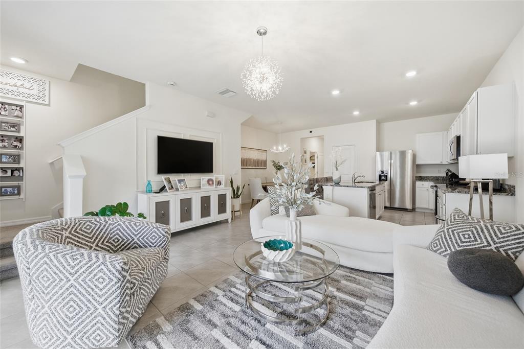 A modern open-concept living room features a white sofa, patterned armchair, and a glass coffee table — 1340 COLT CREEK PLACE, WESLEY CHAPEL, FL