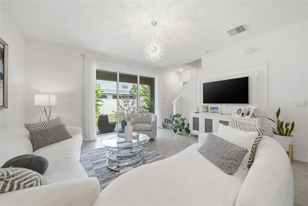 A bright living room features white sofas, a glass coffee table, and a wall-mounted television — 1340 COLT CREEK PLACE, WESLEY CHAPEL, FL