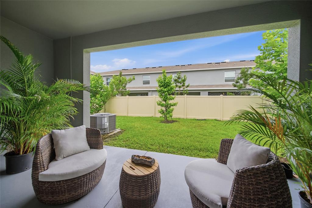 A covered patio features two wicker chairs and a small table overlooking a grassy backyard — 1340 COLT CREEK PLACE, WESLEY CHAPEL, FL
