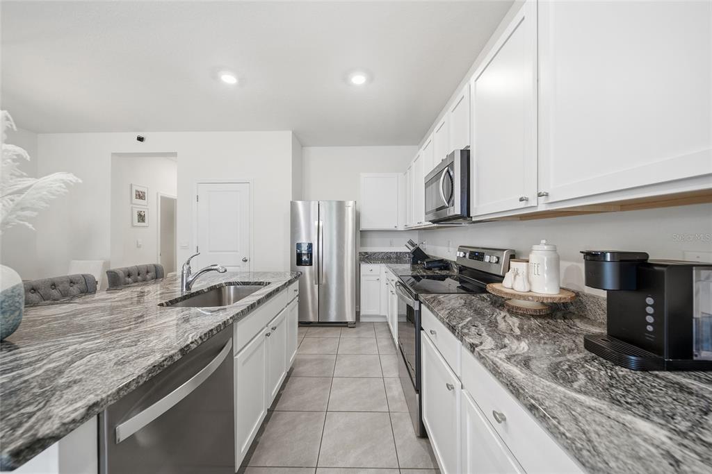 A kitchen features white cabinetry, granite countertops, stainless steel appliances, and tile flooring — 1340 COLT CREEK PLACE, WESLEY CHAPEL, FL