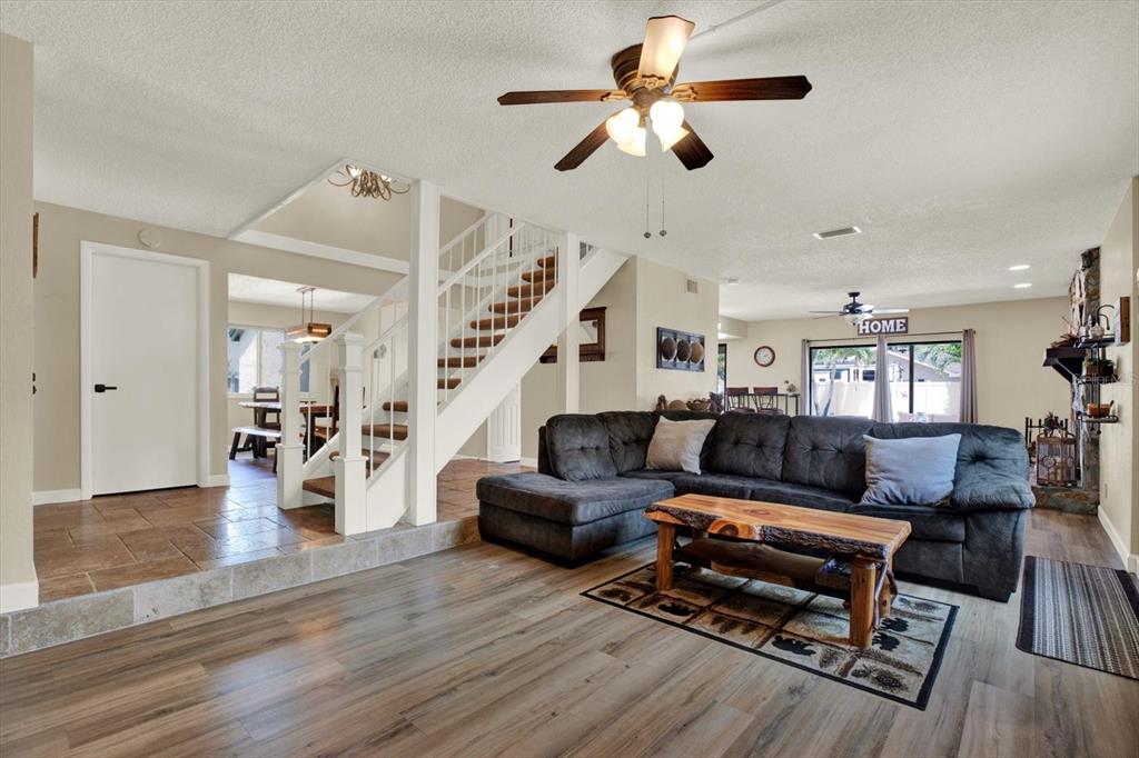 A living room features a sectional sofa, wood-look flooring, a staircase, and a ceiling fan — 7363 ROSETREE PLACE E, SEMINOLE, FL