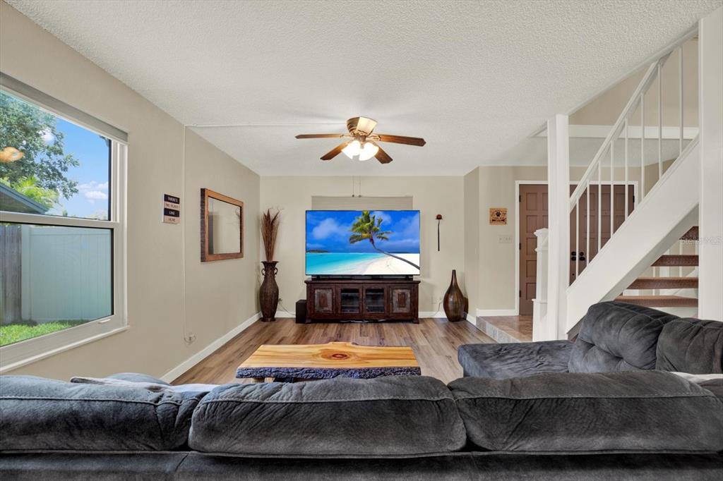 A living room features a grey sectional sofa, a television on a console, and stairs — 7363 ROSETREE PLACE E, SEMINOLE, FL