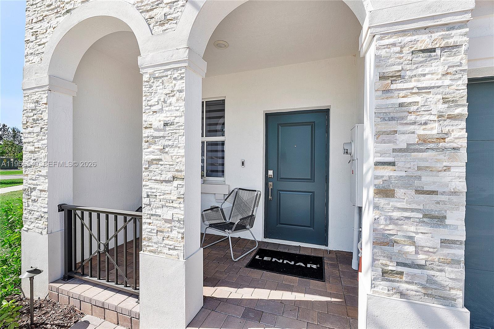 A covered entryway features stone-clad pillars, a dark door, and a paved porch floor — 2361 NW 125th St, Miami FL 33167, MIAMI, FL