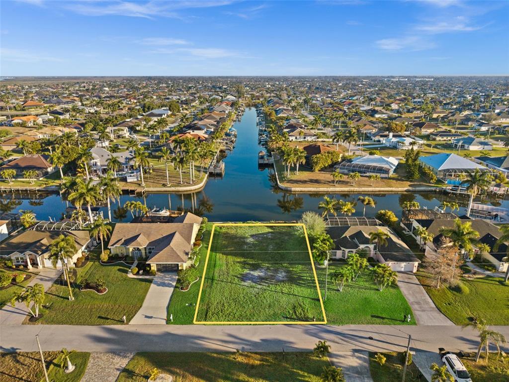 An aerial view shows a vacant waterfront lot outlined in yellow between two residential homes — 2623 SW 35TH LANE, CAPE CORAL, FL