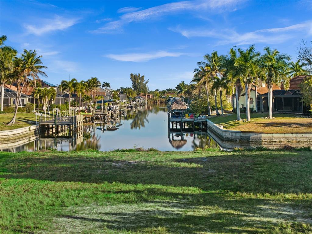 A canal view from a grassy backyard featuring boat docks and palm trees — 2623 SW 35TH LANE, CAPE CORAL, FL