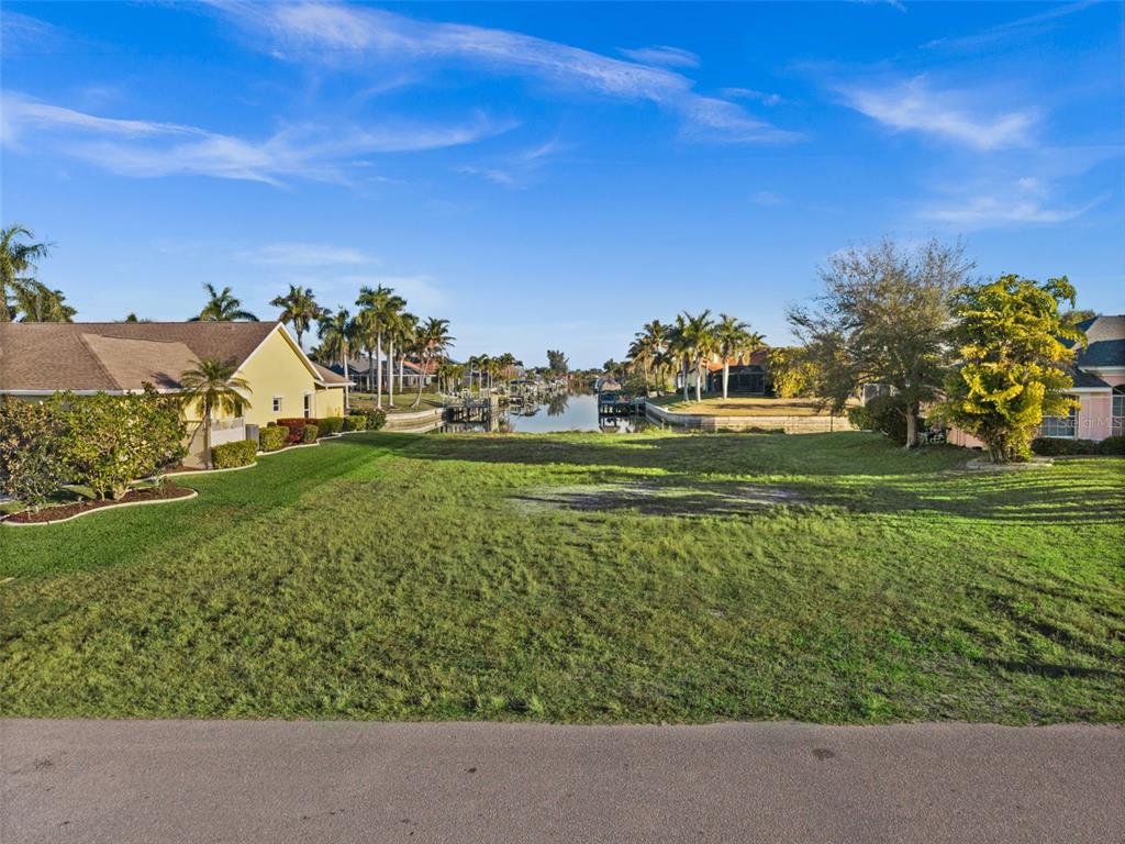 A vacant grassy lot sits between two houses and faces a canal with palm trees — 2623 SW 35TH LANE, CAPE CORAL, FL