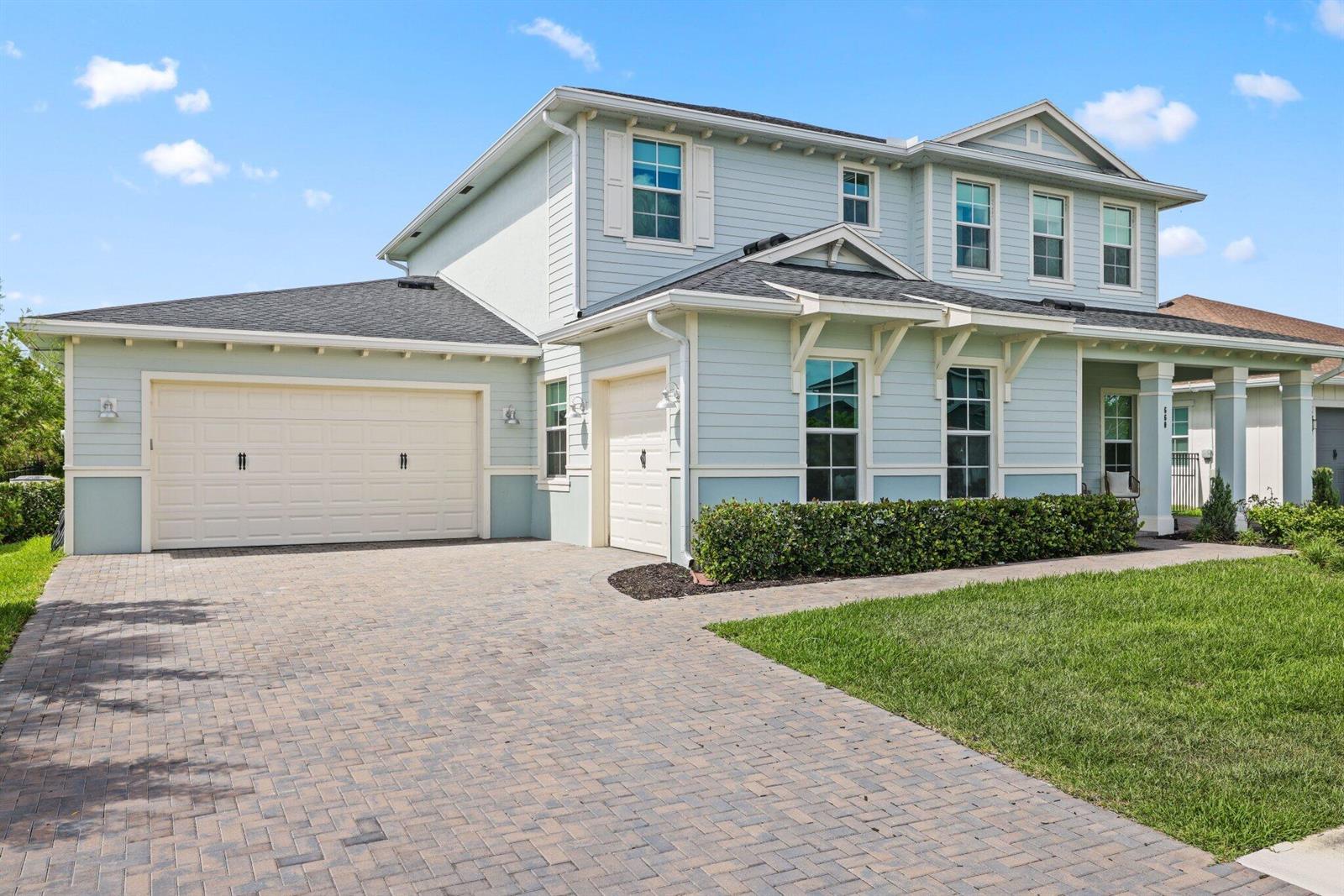 A two-story light blue house features a paver driveway, two garage doors, and a porch — 660 Hookline Circle, Loxahatchee FL 33470, LOXAHATCHEE, FL