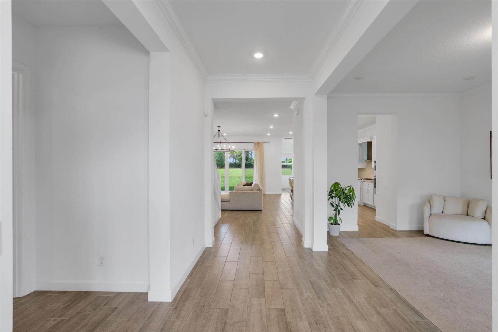 A bright hallway with wood-look tile flooring leads toward a living room and kitchen area — 660 Hookline Circle, Loxahatchee FL 33470, LOXAHATCHEE, FL